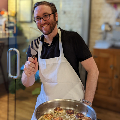 Teddy cooking, wearing an apron, holding up a spatula