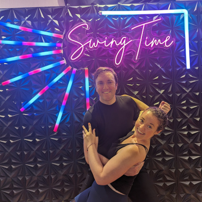 Teddy and his partner Tristine doing a swing dance dip in front of a neon sign